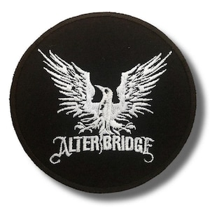 Op de afbeelding: Ronde zwarte patch met een wit geborduurd adelaarsontwerp, vleugels gespreid. De tekst "ALTER BRIDGE" is eronder in het wit geborduurd. Geschikt voor kleding of accessoires.