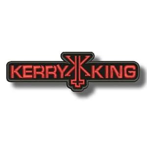 May include: Embroidered patch featuring the name "KERRY KING" in red, with a stylized symbol in the center. The text and symbol are outlined in black. The patch has a rectangular shape with rounded corners.
