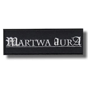 May include: Black rectangular patch with the embroidered text "MARTWA AURA" in white gothic lettering. The patch has a black border and is likely made of fabric.