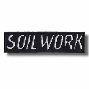 May include: Black rectangular patch with the word "SOIL WORK" embroidered in white, stylized lettering. The patch has a black border and is likely designed to be sewn or ironed onto clothing or accessories.