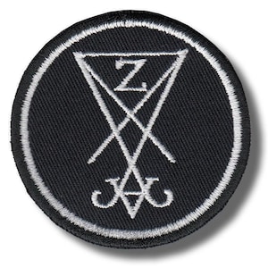 May include: A circular black patch with a white embroidered border. The patch displays a white inverted triangle with a stylized letter "Z" inside, and intersecting lines and symbols.