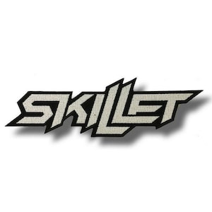 May include: A black and white embroidered patch featuring the word "SKILLET" in a stylized, angular font. The letters are in a light grey color with a black border, creating a bold, eye-catching design. The patch is likely for clothing or accessories.