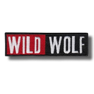 May include: Rectangular embroidered patch with the words "WILD WOLF" in white block letters. The left side of the patch is red, and the right side is black. The patch has a black border.