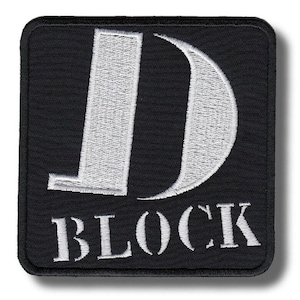 Op de afbeelding: Zwart vierkantige patch met wit geborduurde tekst. De grote letter "D" staat bovenaan, met "BLOCK" eronder. De patch heeft een zwarte rand.