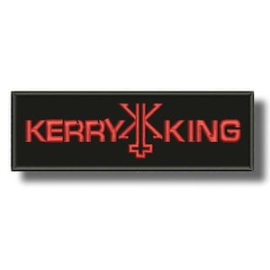 May include: Black rectangular patch with the embroidered text "KERRY KING" in red, with a stylized symbol between the two words. The patch has a black border and a slight shadow.