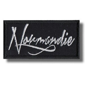 以下が含まれることがあります： 黒い長方形のパッチ。白い筆記体で「Normandie」の文字が刺繍されています。パッチには黒い縁取りがあり、衣類やアクセサリーに縫い付けたり、アイロンで接着したりするように設計されています。
