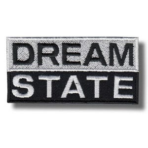 Op de afbeelding: Geborduurde rechthoekige patch met de tekst "DREAM STATE". De tekst is wit, met "DREAM" op een lichtgrijze achtergrond en "STATE" op zwart. De patch heeft een gestikte rand.