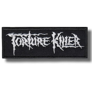 May include: A black rectangular patch featuring the white embroidered text "TORTURE KILLER" in a gothic style. The patch has a black border and is designed for application to clothing or accessories, likely made of fabric.