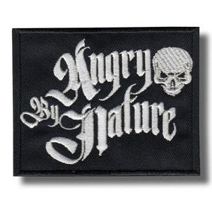 Pode incluir: Patch bordado preto com a frase "Angry by Nature" em escrita gótica, acompanhado por uma caveira. O patch tem formato retangular, com borda preta e fios brancos.