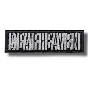 Puede incluir: Un parche rectangular negro con texto bordado blanco "DEATHSAVEN". El parche tiene un borde negro y probablemente está diseñado para ser cosido en ropa o accesorios.