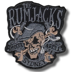 Op de afbeelding: Geborduurde patch met een schedel met piratenhoed, gekruiste zwaarden en de tekst "THE RUMJACKS SYDNEY". De patch is voornamelijk zwart, met grijze, bruine en witte details. Het ontwerp heeft een vintage uitstraling.