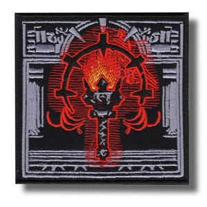 Op de afbeelding: Vierkante zwarte patch met een gedetailleerd geborduurd ontwerp. Het ontwerp heeft een centraal rood embleem met vlamachtige elementen, omgeven door een rode omtrek en grijze architecturale details. De patch heeft een witte rand en een schaduw.