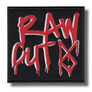 May include: A square black patch featuring the words "RAW CUTS" in red graffiti-style lettering with a white outline. The design is centered on the patch.
