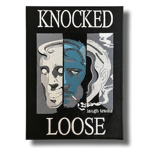 Op de afbeelding: Zwart rechthoekig embleem met de woorden "KNOCKED LOOSE" in witte blokletters. Het embleem toont een afbeelding van een gezicht verdeeld in drie verticale secties, met een blauw-wit kleurenschema. De woorden "laugh tracks" zijn ook zichtbaar.