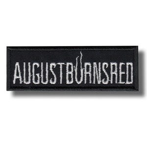 以下が含まれることがあります： 黒い長方形のパッチ。白い文字で「AUGUST BURNS RED」と刺繍されています。パッチには黒い縁取りと影の効果があり、3Dの外観を作り出しています。テキストは様式化されたフォントです。