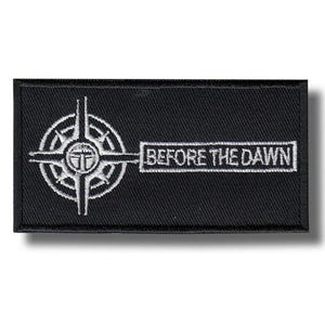 Pode incluir: Patch retangular preto com um design de bússola branca e o texto "BEFORE THE DAWN". A bússola apresenta uma forma de cruz com um emblema central. O texto está em uma fonte limpa e sem serifa.