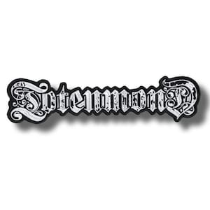 Puede incluir: Un parche bordado en blanco y negro con la palabra "Intenmond" en una fuente gótica. El parche tiene un borde negro y letras blancas, con remolinos decorativos en cada extremo. El parche es de forma rectangular.