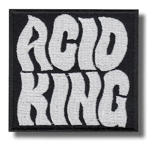 May include: Black square patch with white embroidered text that reads "ACID KING" in a bold, stylized font. The patch has a black border and a shadow effect, giving it a three-dimensional appearance. The text is the primary focus.