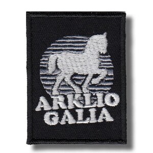 Può includere: Toppa rettangolare nera con una silhouette di cavallo ricamata in bianco all'interno di un cerchio a strisce. Il testo "ARKLIO GALIA" è ricamato in bianco sotto. La toppa ha un bordo nero.