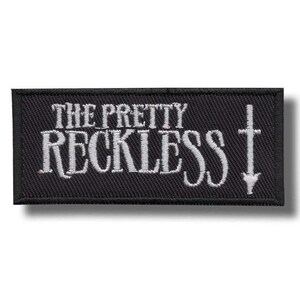 Op de afbeelding: Een rechthoekige zwarte patch met witte geborduurde tekst "THE PRETTY RECKLESS". Een wit kruis met een pijl naar beneden staat rechts. Geschikt voor kleding of accessoires.