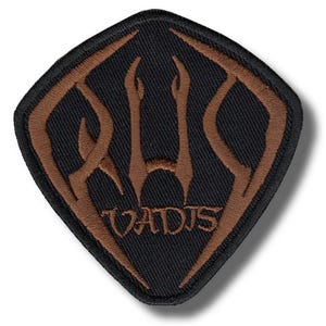 Op de afbeelding: Zwart en bruin geborduurde patch in een ruitvorm. De patch heeft een bruin gestileerd ontwerp en het woord "VADIS" in bruin geborduurd aan de onderkant. Geschikt voor kleding of accessoires.