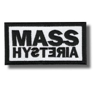 Puede incluir: Un parche rectangular con las palabras "MASS HYSTERIA" en letras negras y en negrita sobre un fondo blanco. El texto está reflejado debajo. El parche tiene un borde negro.