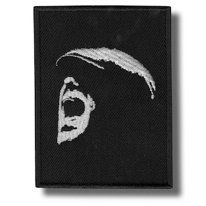 Op de afbeelding: Zwart geborduurde patch met een wit, gestileerd beeld van een schreeuwend gezicht. De patch heeft een rechthoekige vorm met een zwarte rand en een textuur van stof. Het ontwerp is een minimalistische, grafische weergave.