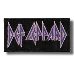 以下が含まれることがあります： 黒い長方形のパッチ。バンド名「DEF LEPPARD」が、ラベンダーとライトグレーの糸で刺繍された、様式化された角張ったフォントで表示されています。このパッチは、衣類やアクセサリーに縫い付けるように設計されています。