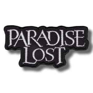 Puede incluir: Parche bordado negro con las palabras "PARADISE LOST" en blanco. El texto está escrito en una fuente gótica. El parche tiene un borde negro y una forma rectangular con un borde inferior irregular.