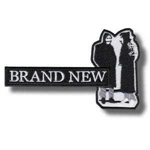 Könnte beinhalten: Schwarz-weißer, gestickter Aufnäher mit dem Text "BRAND NEW" in weißen Buchstaben. Der Aufnäher zeigt eine stilisierte Abbildung von zwei Figuren in Silhouette.