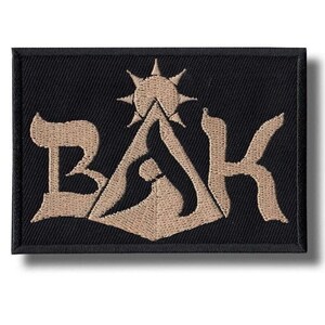 Può includere: Toppa rettangolare nera con la scritta "BAK" in lettere beige stilizzate. Il design include un sole e forme simili a montagne. La toppa è probabilmente per abbigliamento o accessori.