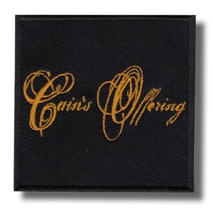 Peut inclure: Écusson carré noir avec texte doré brodé « Cain's Offering » en écriture cursive. L'écusson a une bordure noire et un léger effet d'ombre.