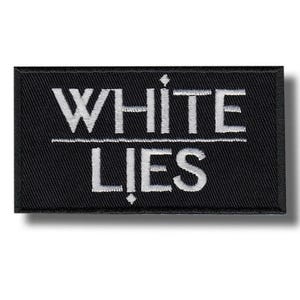 Puede incluir: Un parche rectangular negro con las palabras "WHITE" sobre "LIES" en blanco, con fuente sans-serif. Una línea blanca horizontal separa las dos palabras. El parche tiene una textura tejida.