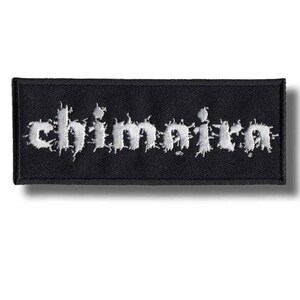 Puede incluir: Un parche rectangular negro con la palabra "Chimaira" bordada en blanco, con letras estilizadas y desgastadas. El parche tiene un borde negro y probablemente está diseñado para ser cosido en ropa o accesorios.