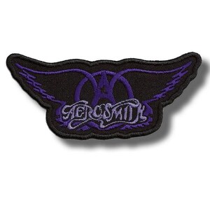 Pode incluir: Patch dos Aerosmith com o logotipo da banda: um emblema alado estilizado com o nome da banda em itálico. O patch tem um fundo preto com asas e letras roxas. O patch tem aproximadamente 10 cm de largura.