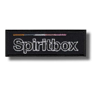 Peut inclure: Un écusson rectangulaire noir avec le mot "Spiritbox" brodé en blanc, bordé d'un fin liseré noir. Au-dessus du texte se trouve une fine ligne horizontale avec des fils orange, blancs et roses.