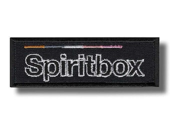 May include: A black rectangular patch with the word "Spiritbox" embroidered in white, outlined with a thin black border. Above the text is a thin horizontal line with orange, white, and pink threads.