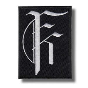 May include: Black rectangular patch featuring a white embroidered gothic letter "F". The letter is in a stylized font with serifs and a curved design element. The patch has a black border, suitable for sewing or ironing on.