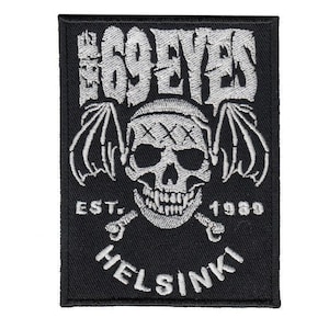 May include: Black rectangular patch with white embroidered text and imagery. The text reads "THE 69 EYES" above a skull with bat wings, crossed bones, and the text "EST. 1989 HELSINKI".
