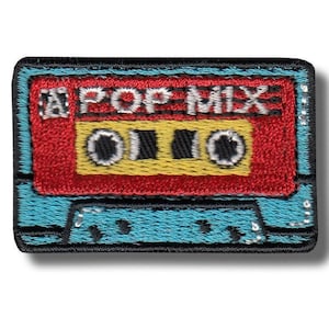 Pode incluir: Patch bordado em forma de fita cassete. O patch apresenta um centro vermelho com as palavras "POP MIX" em branco. Os detalhes da fita são amarelos e pretos, com uma borda turquesa e contorno preto.