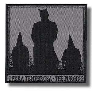 Peut inclure: Écusson noir et gris représentant trois silhouettes sur fond gris. La figure centrale a une tête cornue, flanquée de deux figures en capuches pointues. Le texte "TERRA TENEBROSA - THE PURGING" est en bas.