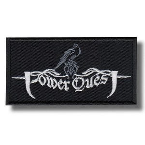 Puede incluir: Parche rectangular negro con texto bordado en blanco y un emblema de pájaro. El texto dice "Power Quest" en una fuente estilizada, con un pájaro posado encima. El parche tiene un borde negro.