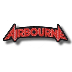 Peut inclure: Un écusson noir avec le mot "AIRBOURNE" en rouge, avec des coutures blanches. Le texte est dans une police stylisée et sur fond noir. L'écusson a la forme d'une flèche.