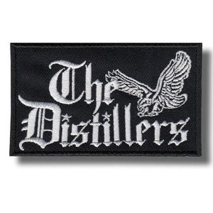 May include: Black rectangular patch featuring white embroidered text and a flying bird graphic. The text reads "The Distillers" in a gothic font. The bird is shown with outstretched wings.