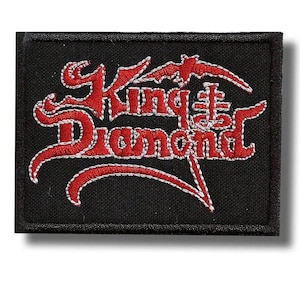 May include: Black rectangular patch with the words "King Diamond" embroidered in red with white stitching. A bat-like shape is above the word "King". The patch has a black border.
