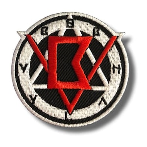 May include: Embroidered patch with a black background and a white border. The patch features a red geometric design in the center, surrounded by white triangles and letters. The patch is round and has a textured appearance.