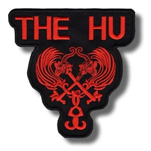 Puede incluir: Parche bordado negro con el texto "THE HU" en rojo. Debajo, un emblema rojo con dos dragones estilizados y lanzas cruzadas. El parche tiene una forma única y puede ser cosido en ropa.