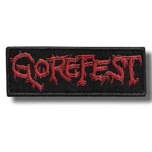 Puede incluir: Parche rectangular negro con la palabra "GOREFEST" bordada en rojo, con letras estilizadas. El parche tiene un borde negro y está diseñado para ser cosido o planchado en ropa o accesorios. El texto está en una fuente gótica.