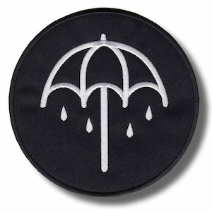 May include: A circular black patch with a white umbrella and water droplet design. The umbrella is a simple outline. This patch is likely for application on clothing or accessories.