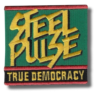 Op de afbeelding: Geborduurde patch met de woorden "FEEL PULSE" in gouddraad op een groene achtergrond. De patch bevat ook de tekst "TRUE DEMOCRACY" in zwart en goud. De patch heeft een rode rand.